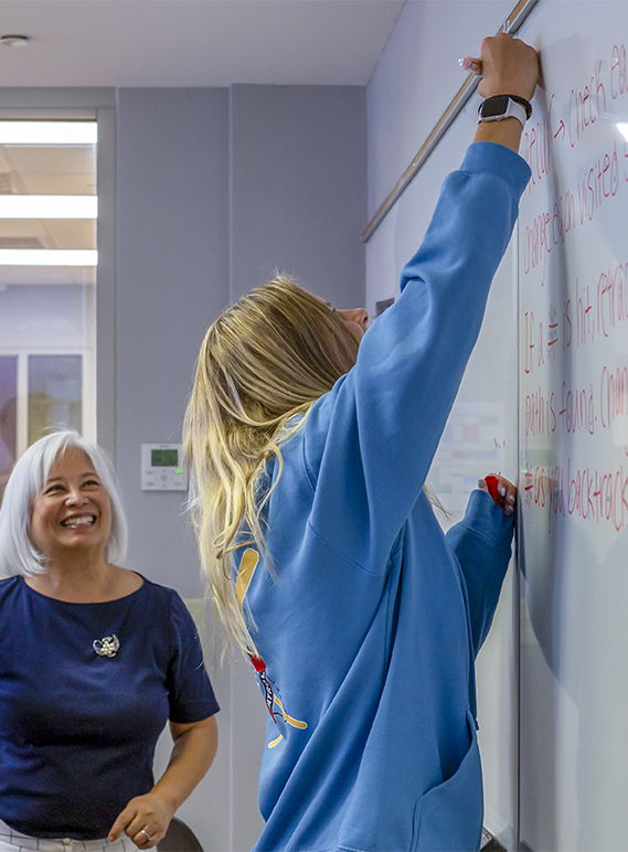 Joy Wolfe smiling teaching a female student computer science on a whiteboard
