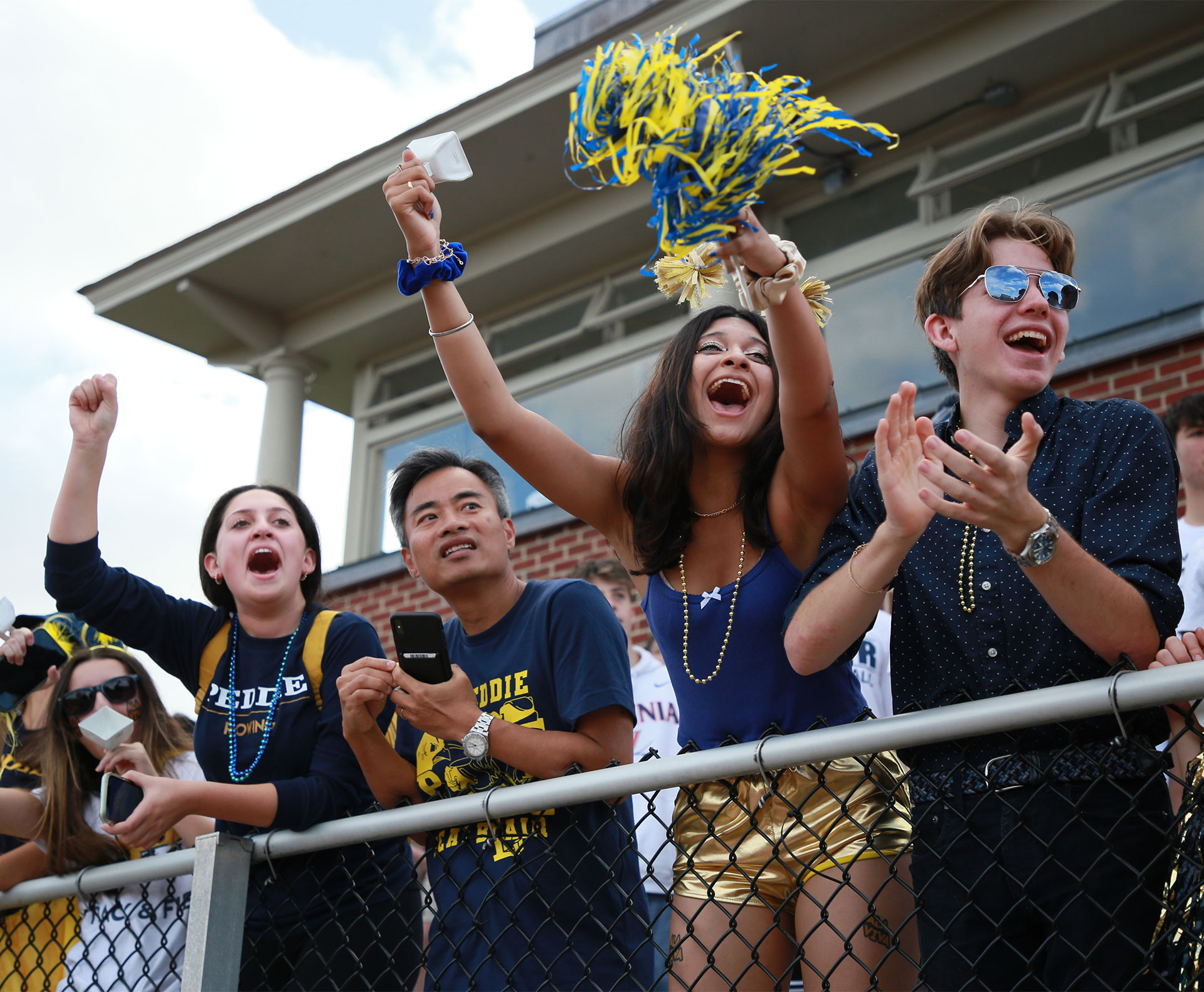 students and adults cheering on the sidelines dressed in blue and gold